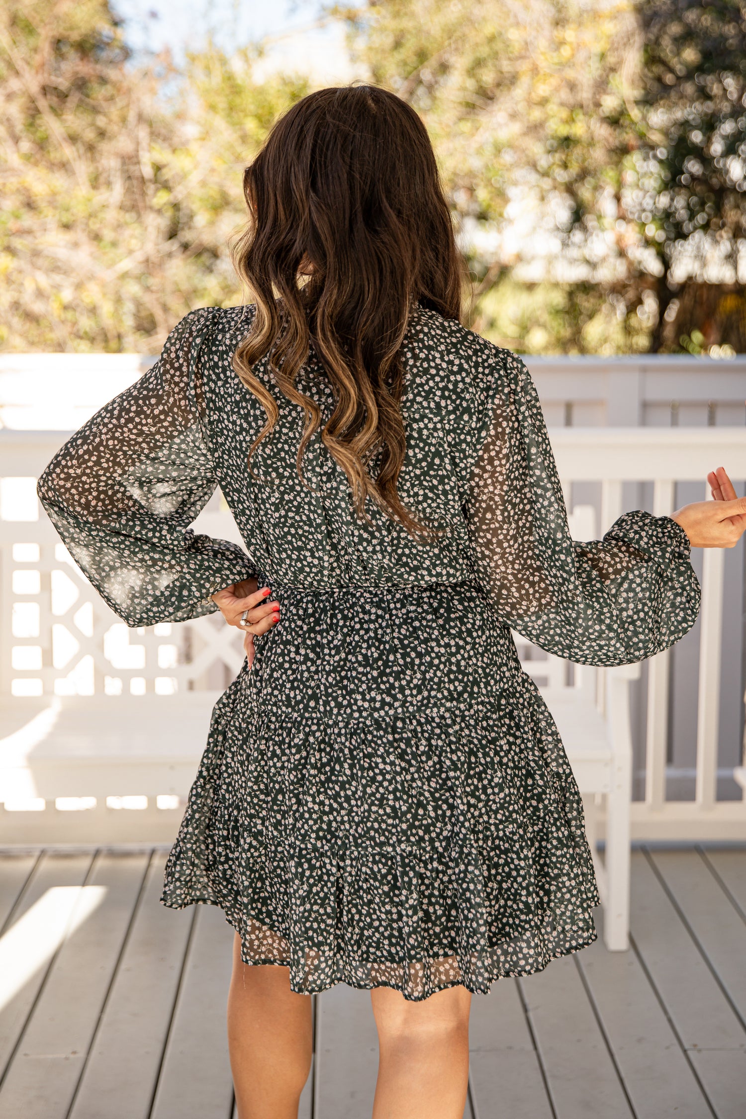Woman wearing a floral dress on a wooden deck with trees in the background