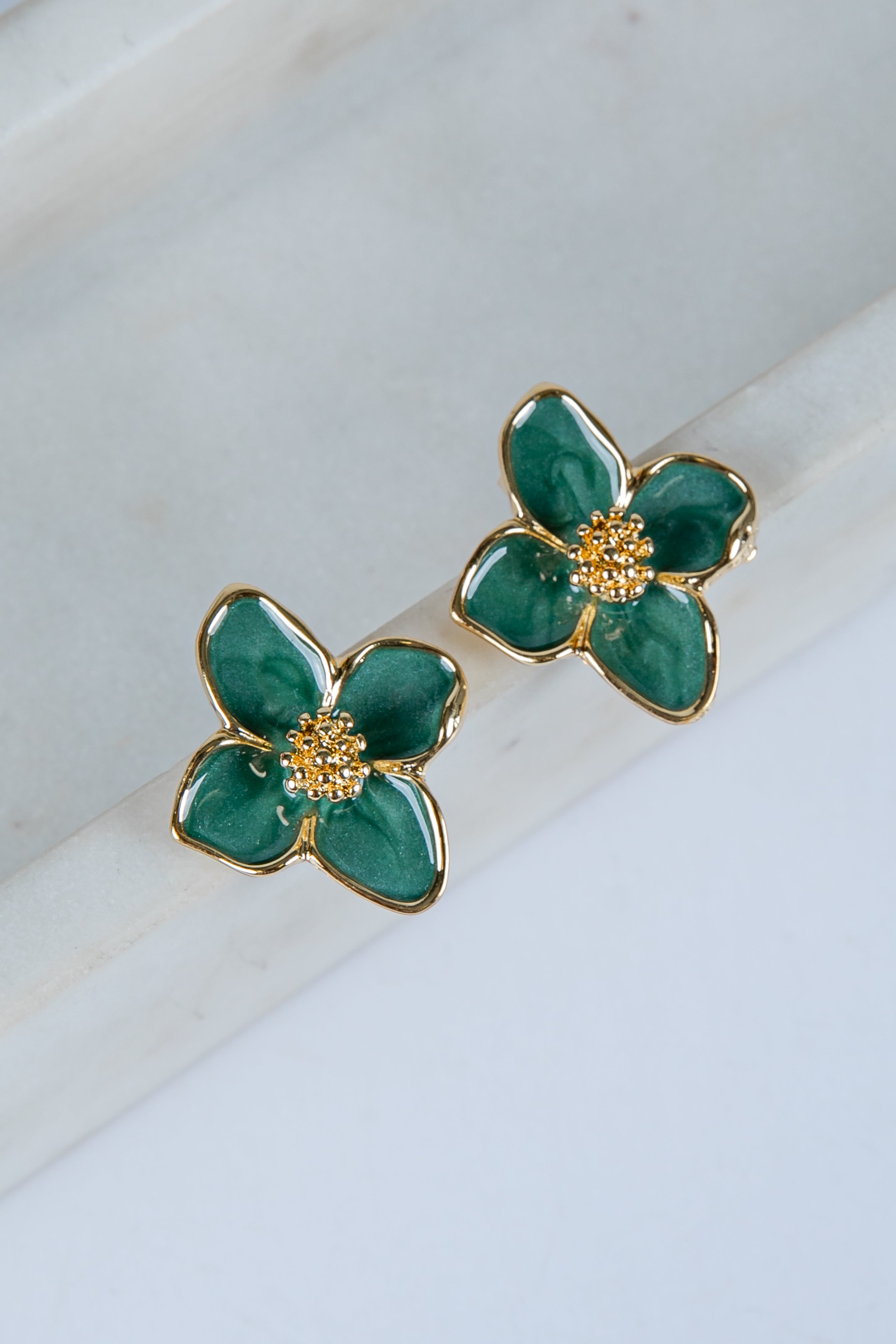 Green flower-shaped earrings with gold accents on a marble surface
