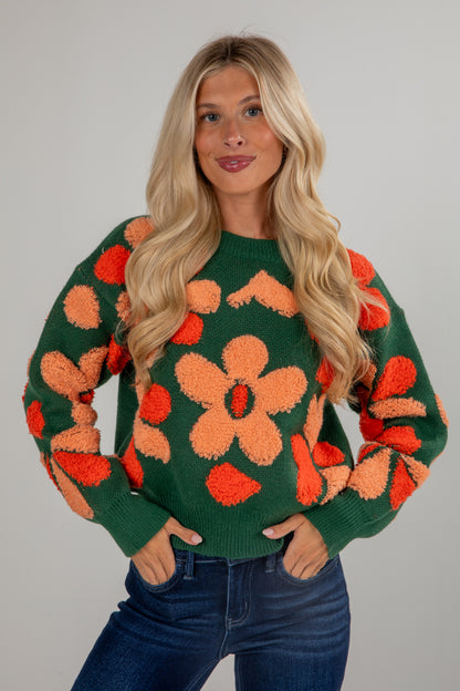 Woman wearing a green sweater with orange floral patterns on a gray background