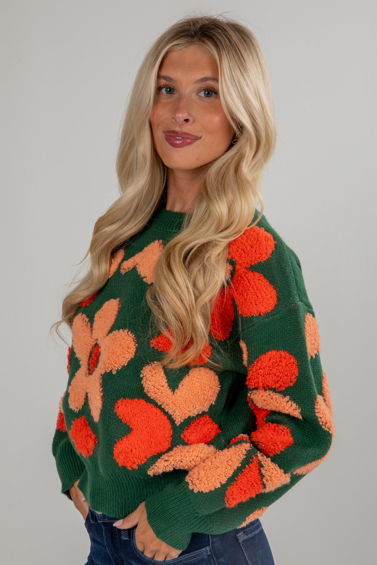 Woman wearing a green sweater with orange floral patterns on a gray background