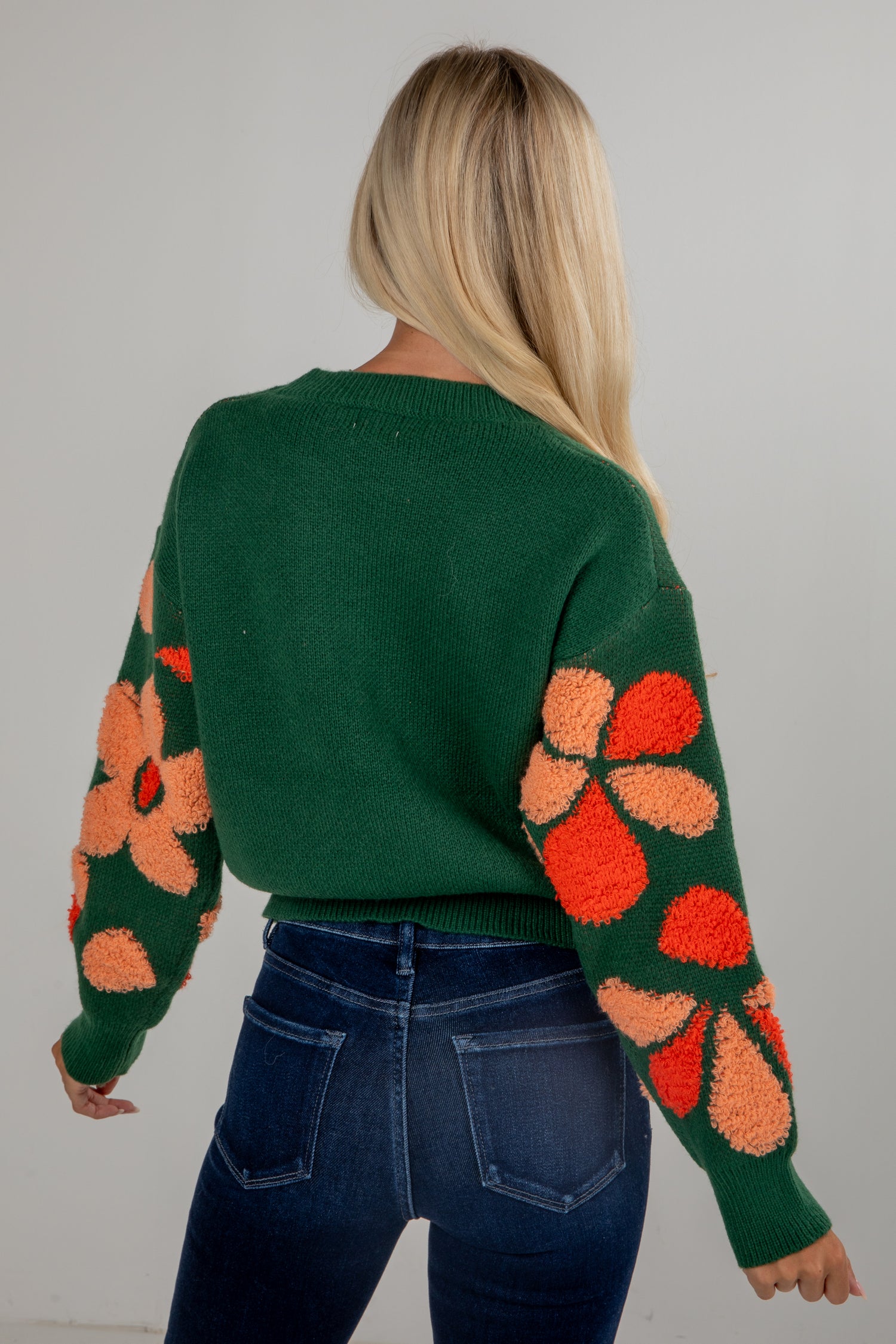 Person wearing a green sweater with colorful floral patterns on a plain background