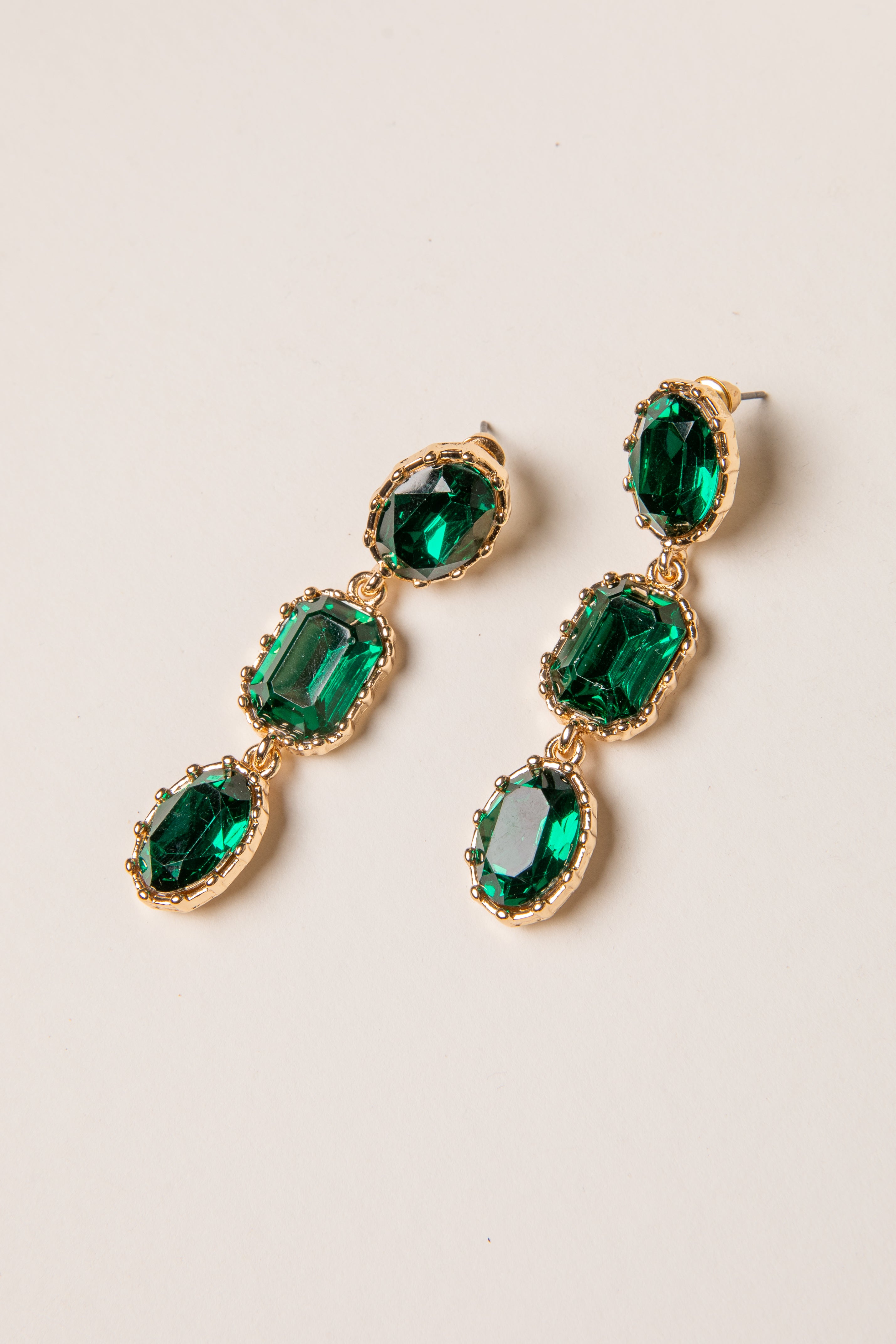 Green gemstone earrings with gold accents on a beige background