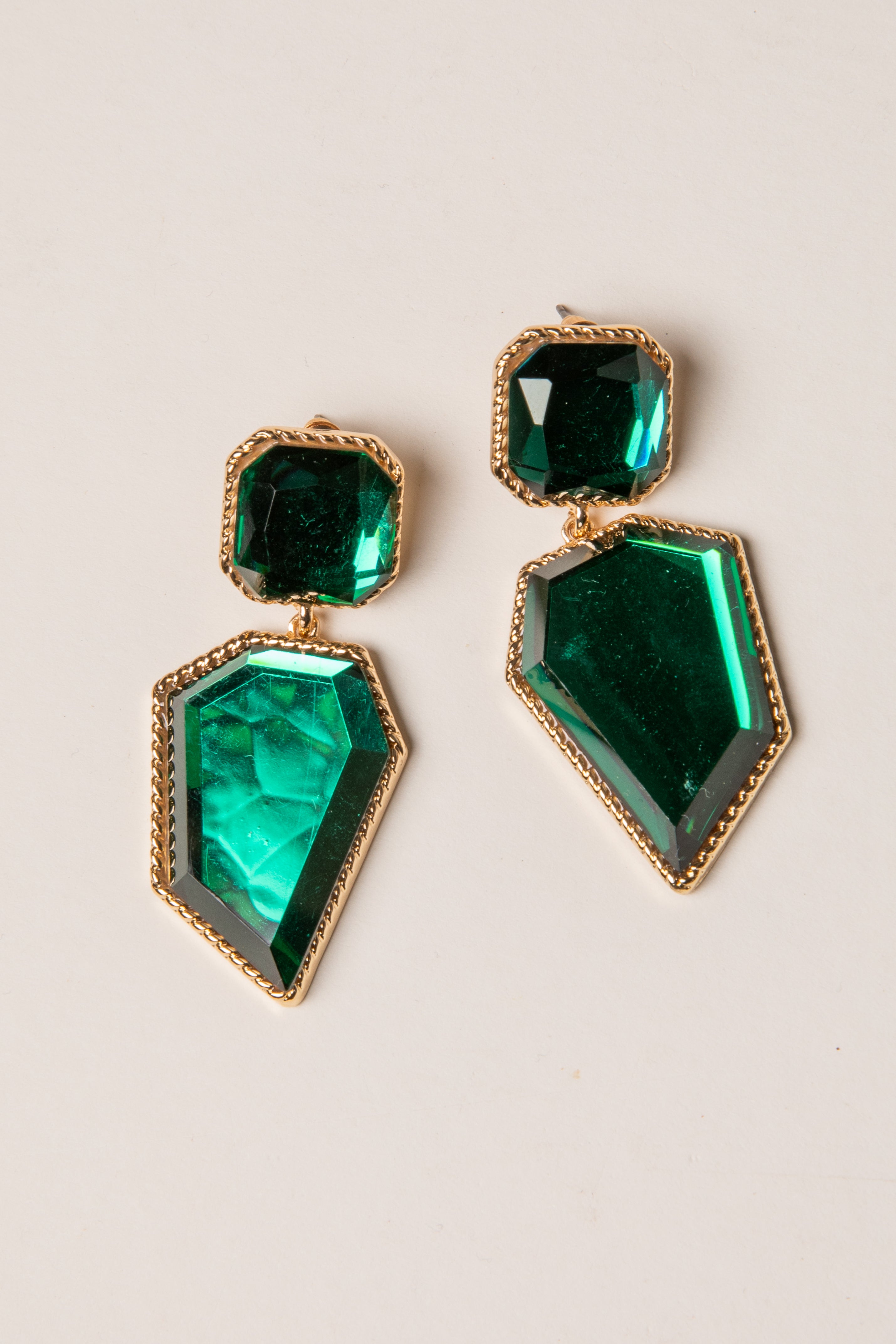 Green gemstone earrings with gold accents on a beige background
