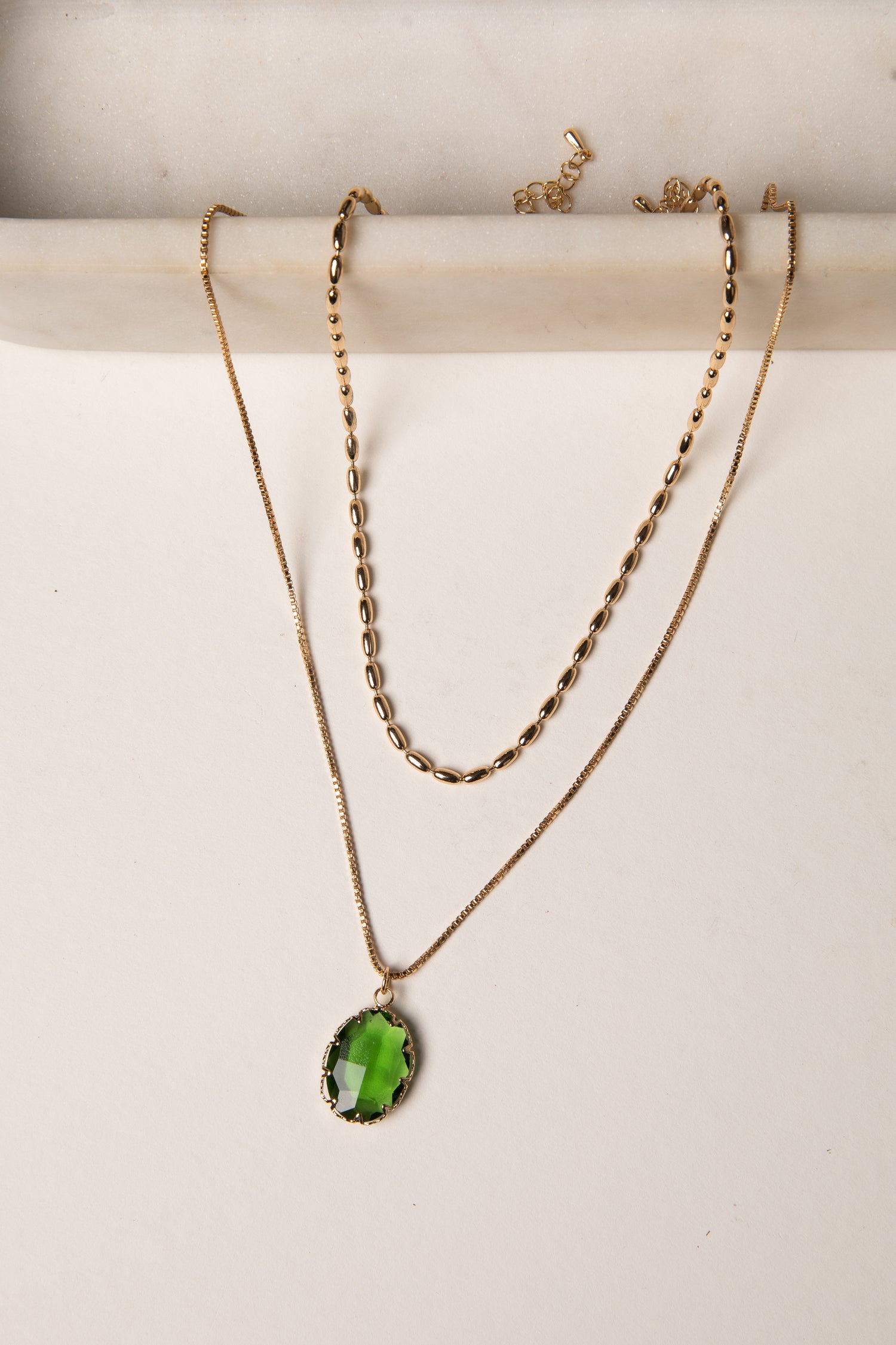 Two gold necklaces with green pendants on a white background