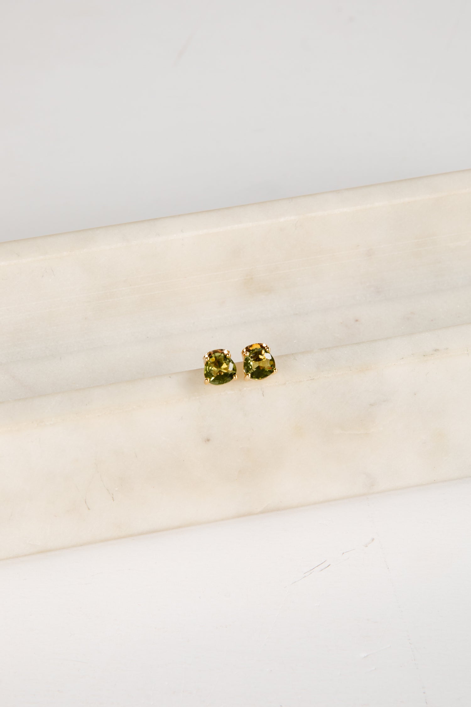 Pair of green gemstone stud earrings on a white marble surface
