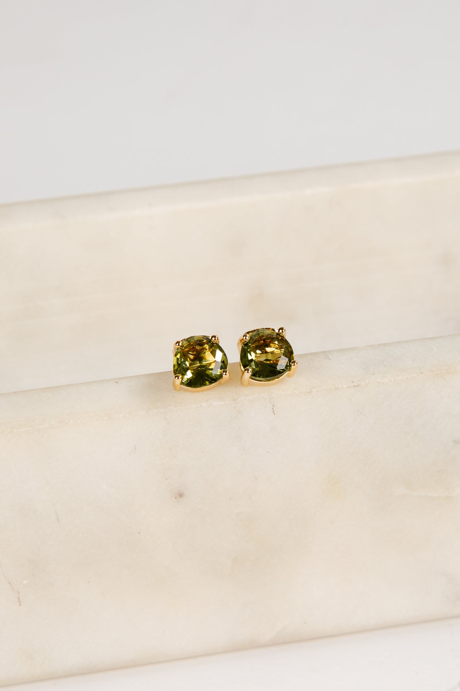 Gold earrings with green gemstones on a beige surface
