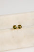 Gold earrings with green gemstones on a beige surface