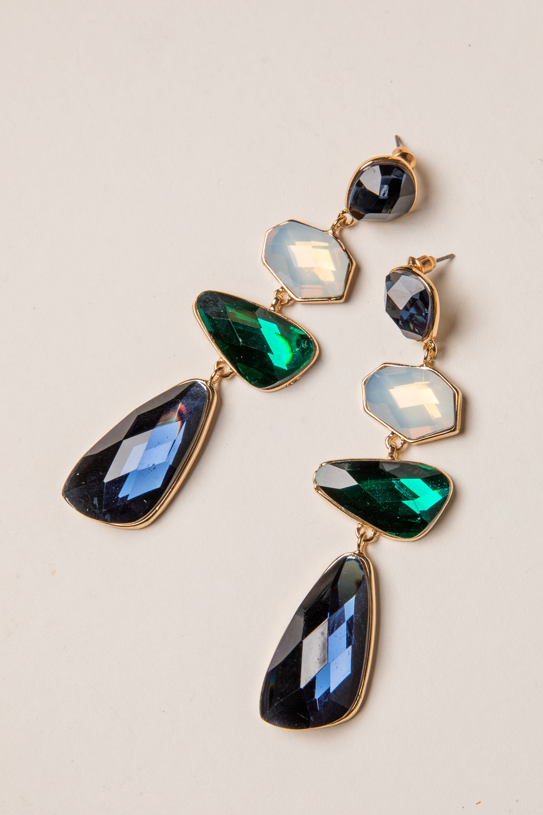 Pair of gold earrings with green and blue gemstones on a light background