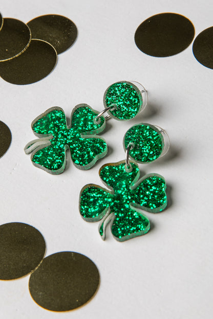 Green glittery shamrock earrings on a white background with gold coins.