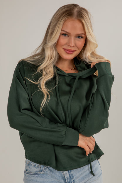 Woman wearing a green hoodie and blue jeans against a plain background