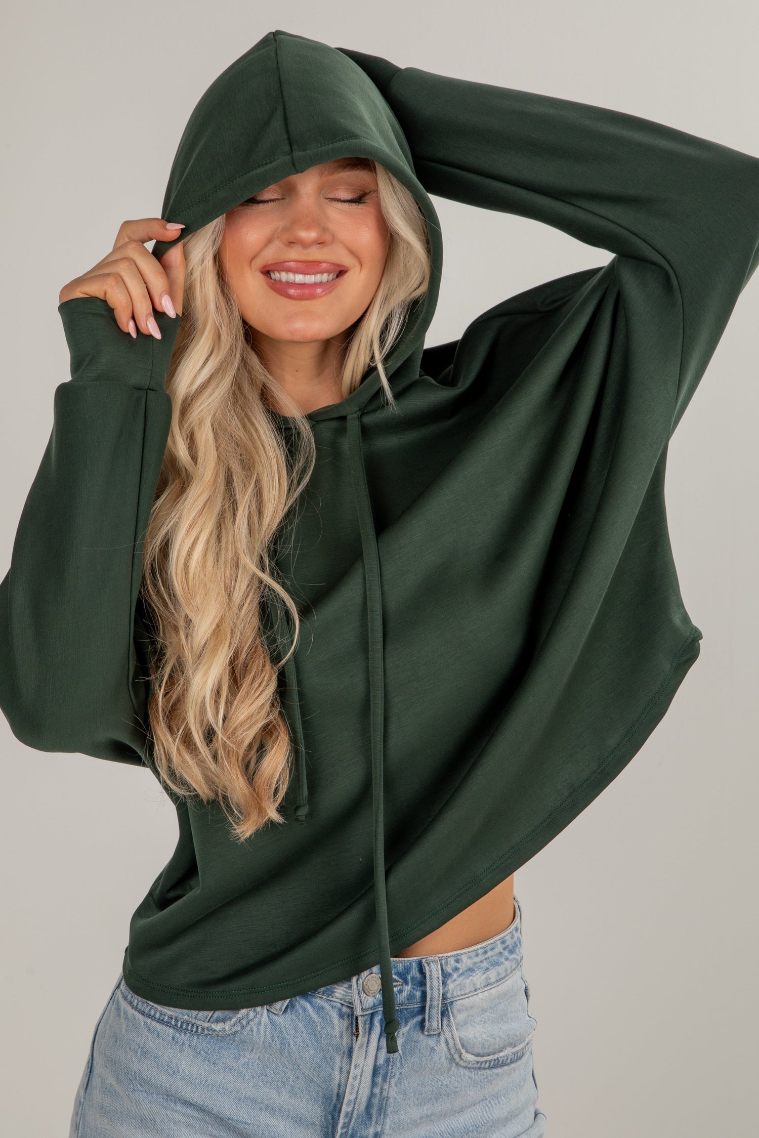 Woman wearing a green hoodie and blue jeans against a plain background