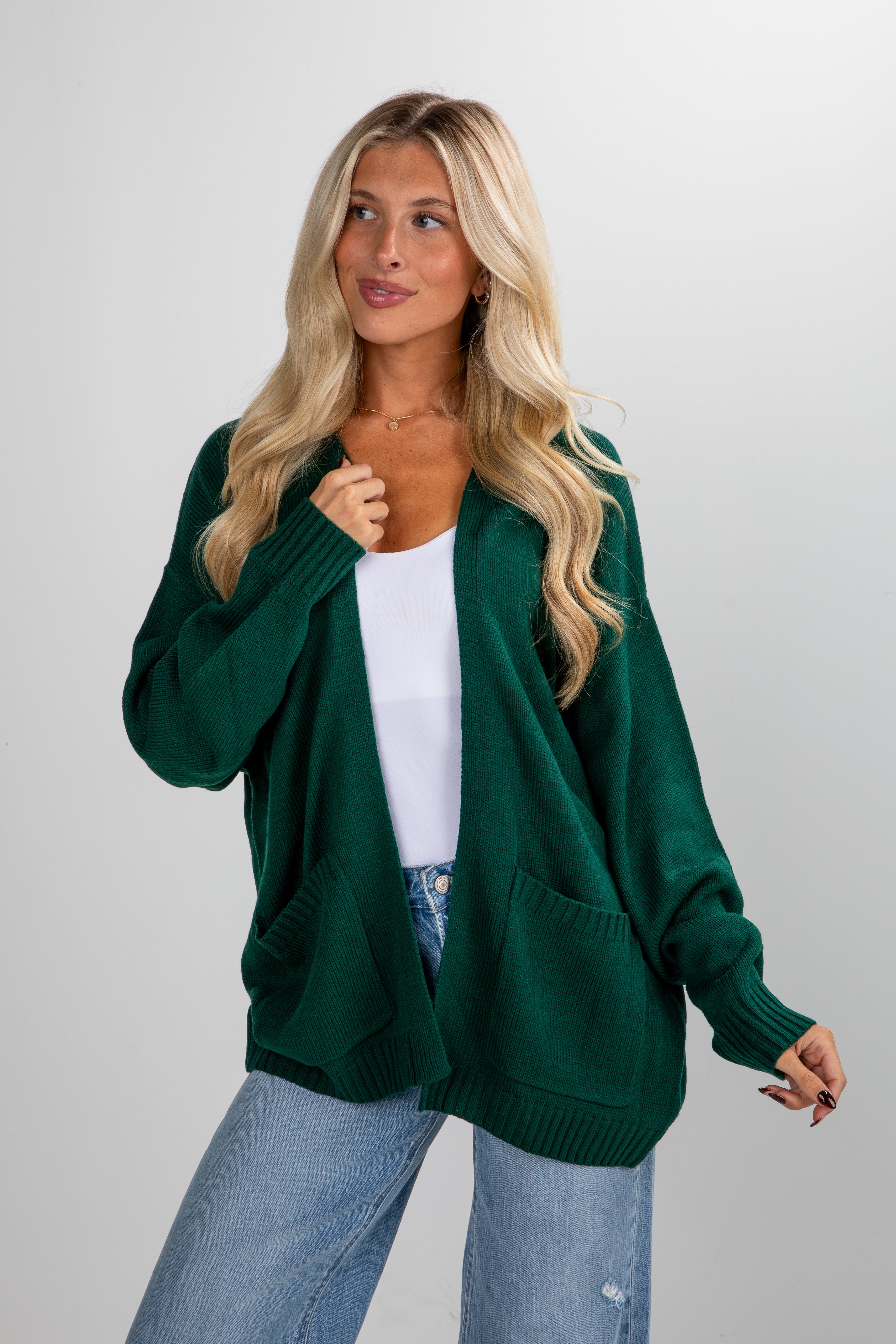 Woman wearing a green cardigan over a white top and blue jeans on a plain background