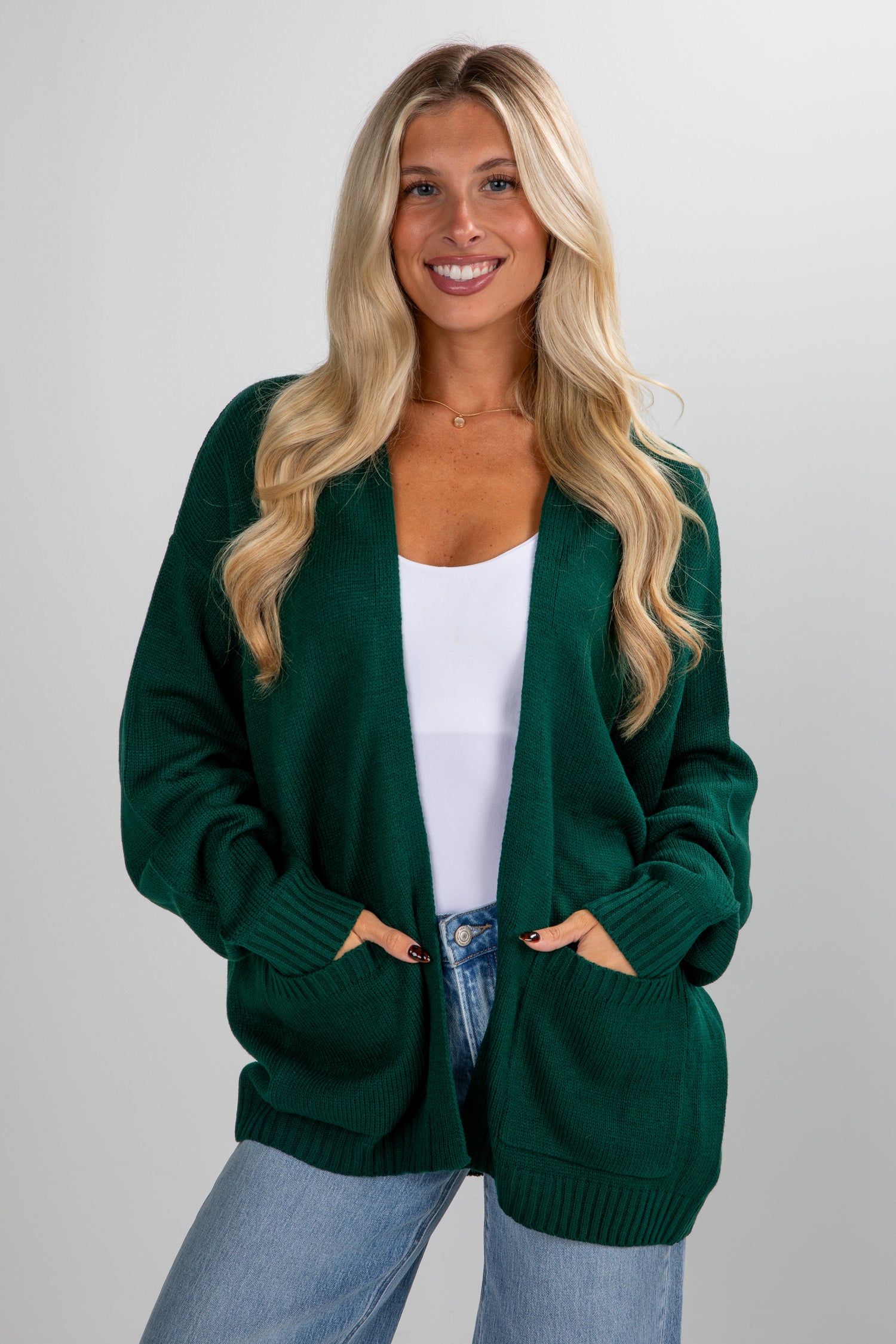 Woman wearing a green cardigan over a white top and blue jeans on a plain background