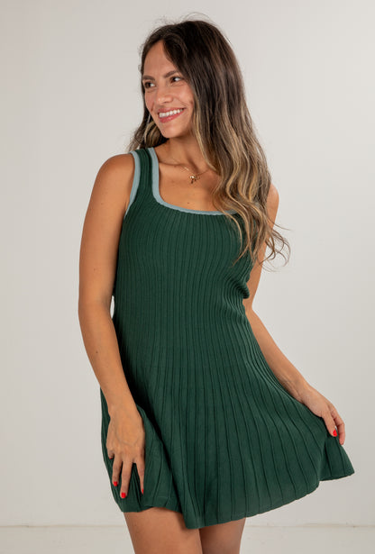 Woman wearing a green ribbed dress against a plain background