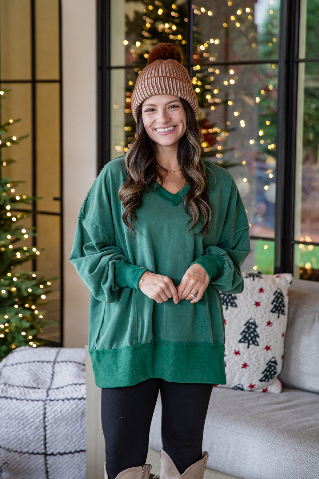 Woman wearing a green sweater and brown beanie standing in a room with Christmas decorations.