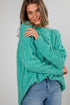 Woman wearing a teal sweater and blue jeans against a plain background