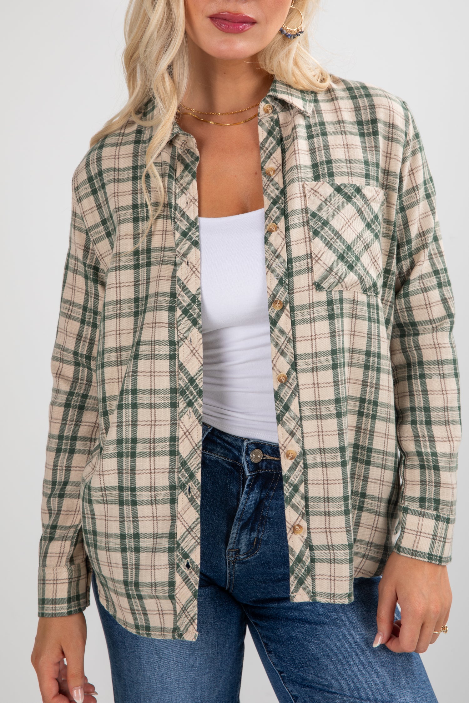 Woman wearing a plaid shirt over a white top and blue jeans on a plain background