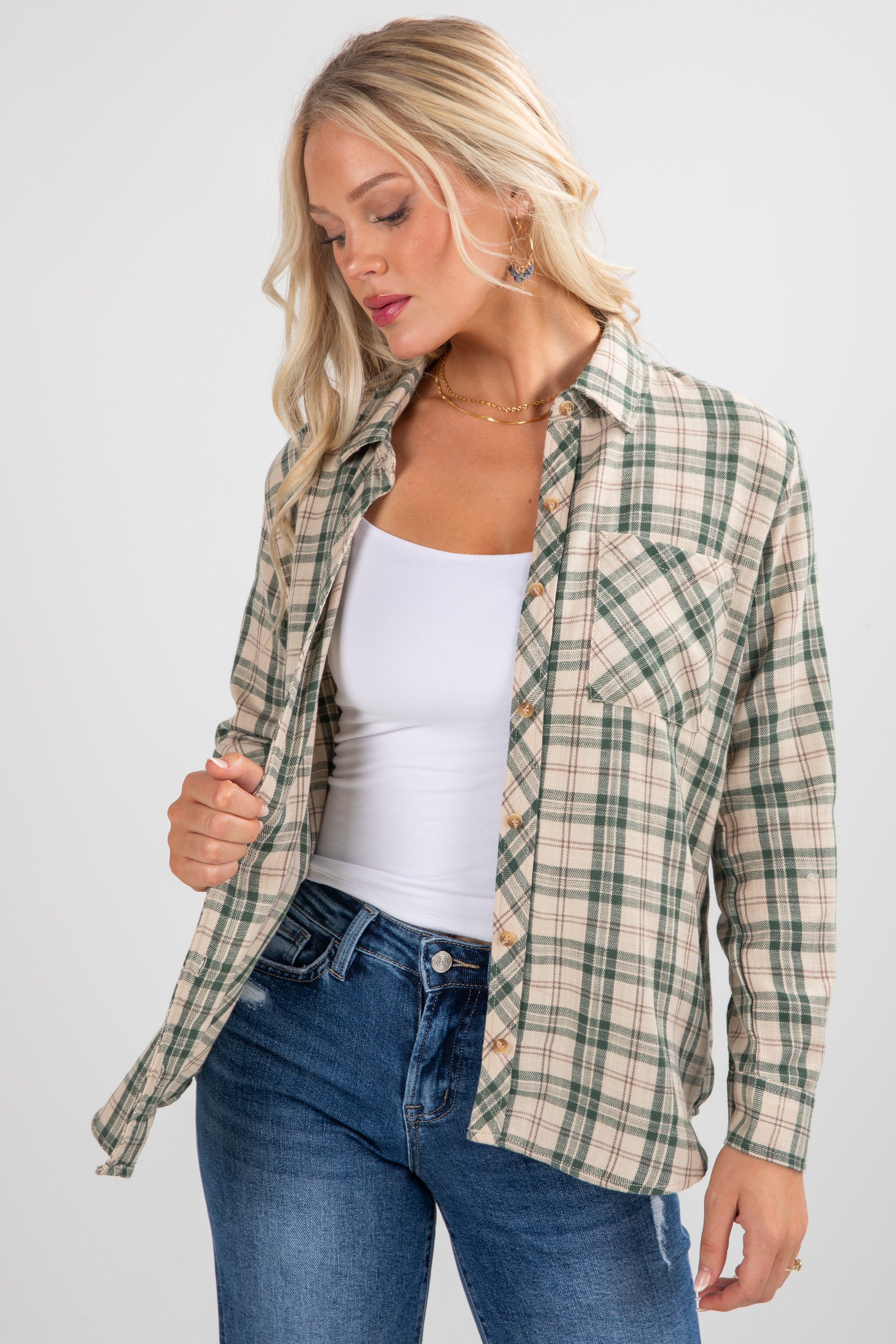 Woman wearing a plaid shirt over a white top and blue jeans on a light gray background