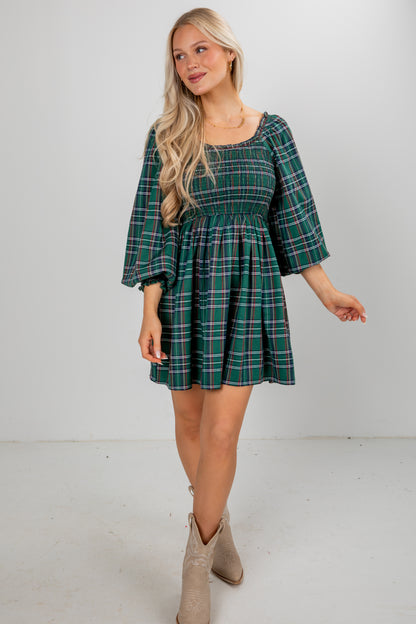 Woman wearing a green plaid dress with beige boots on a white background