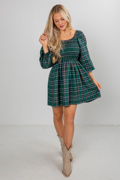 Woman wearing a green plaid dress with beige boots on a white background