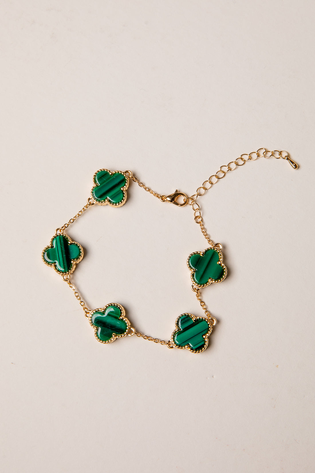 Gold bracelet with green clover-shaped charms on a beige background