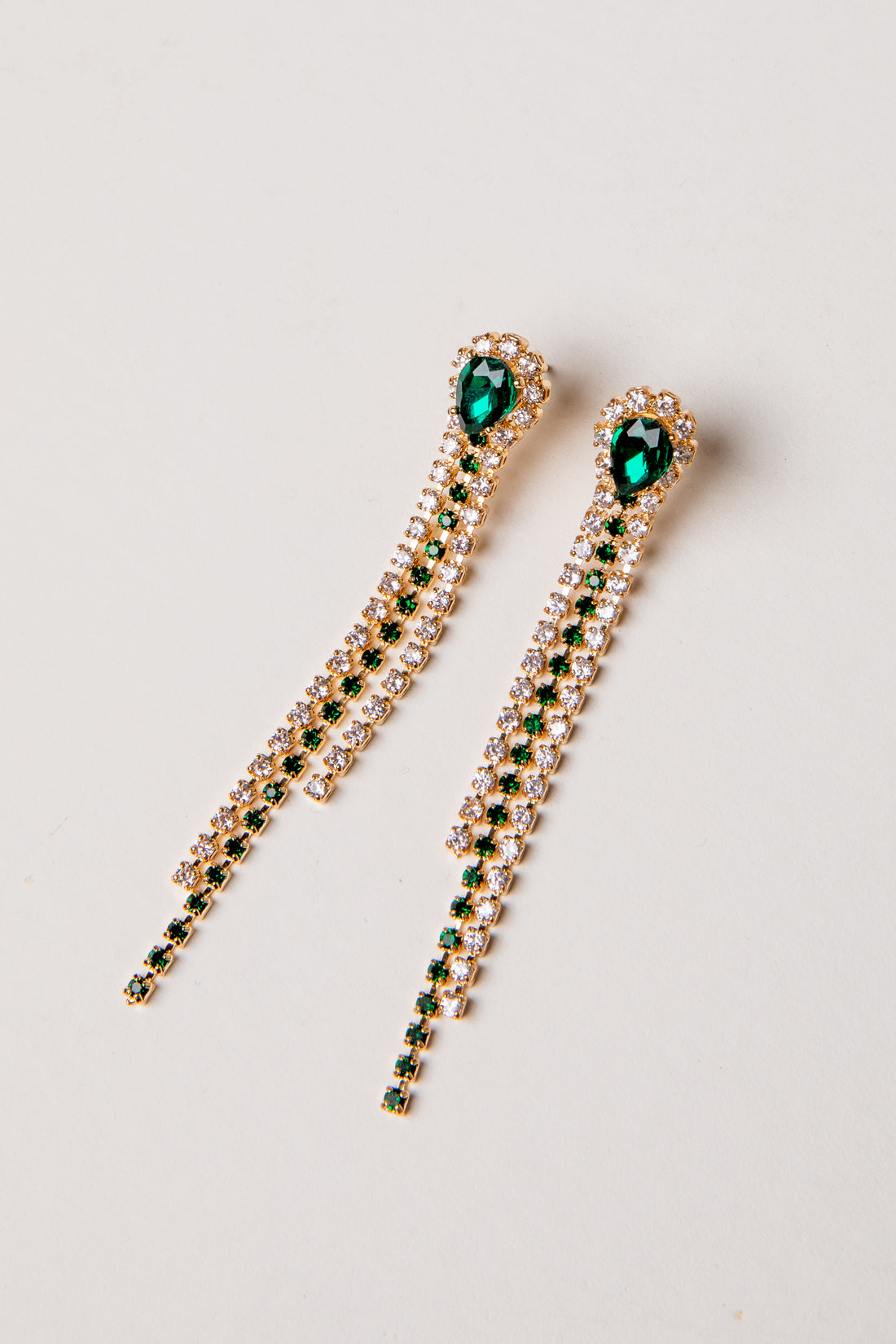 Pair of gold earrings with green gemstones on a light gray background
