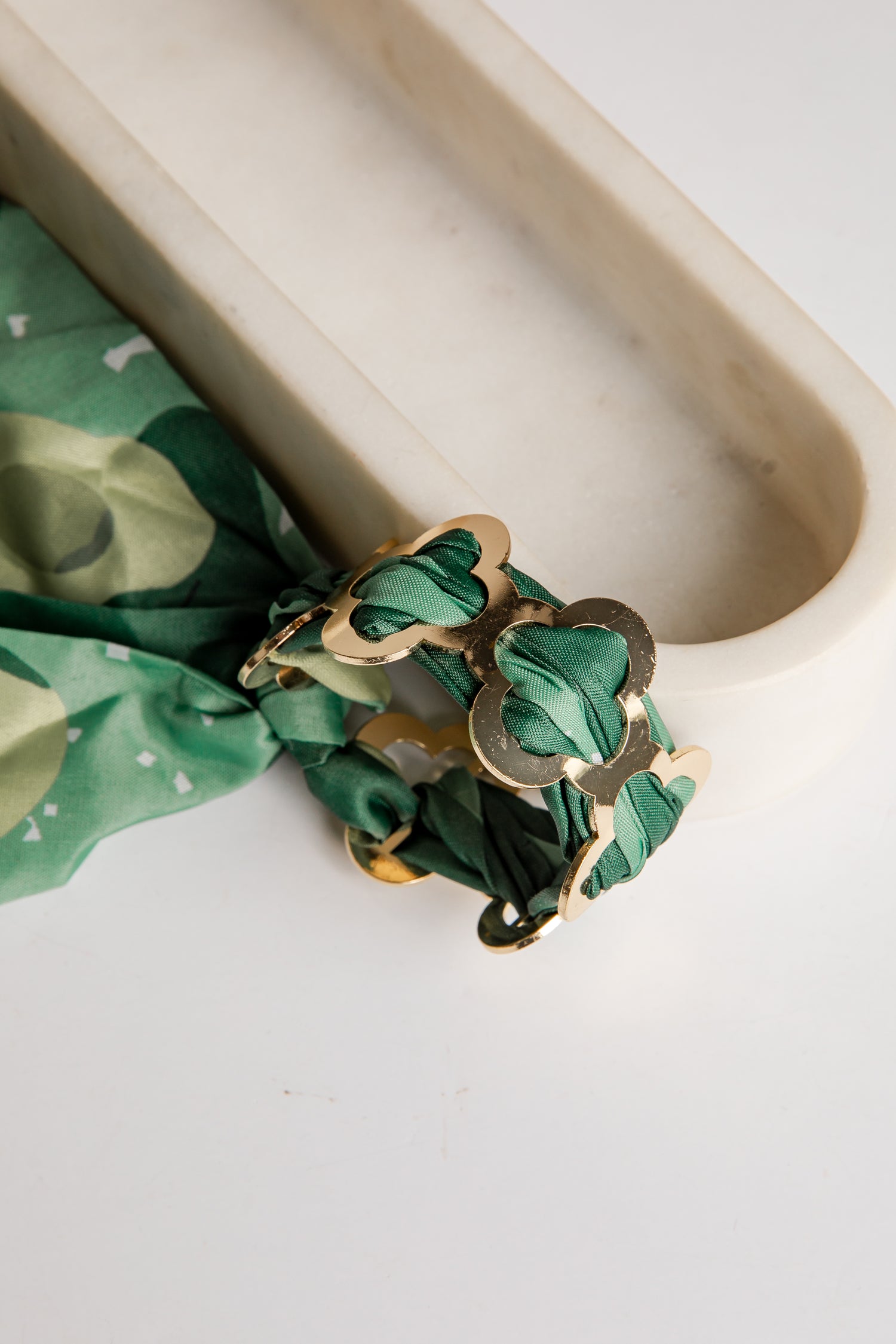 Gold bracelet with green fabric on a white surface