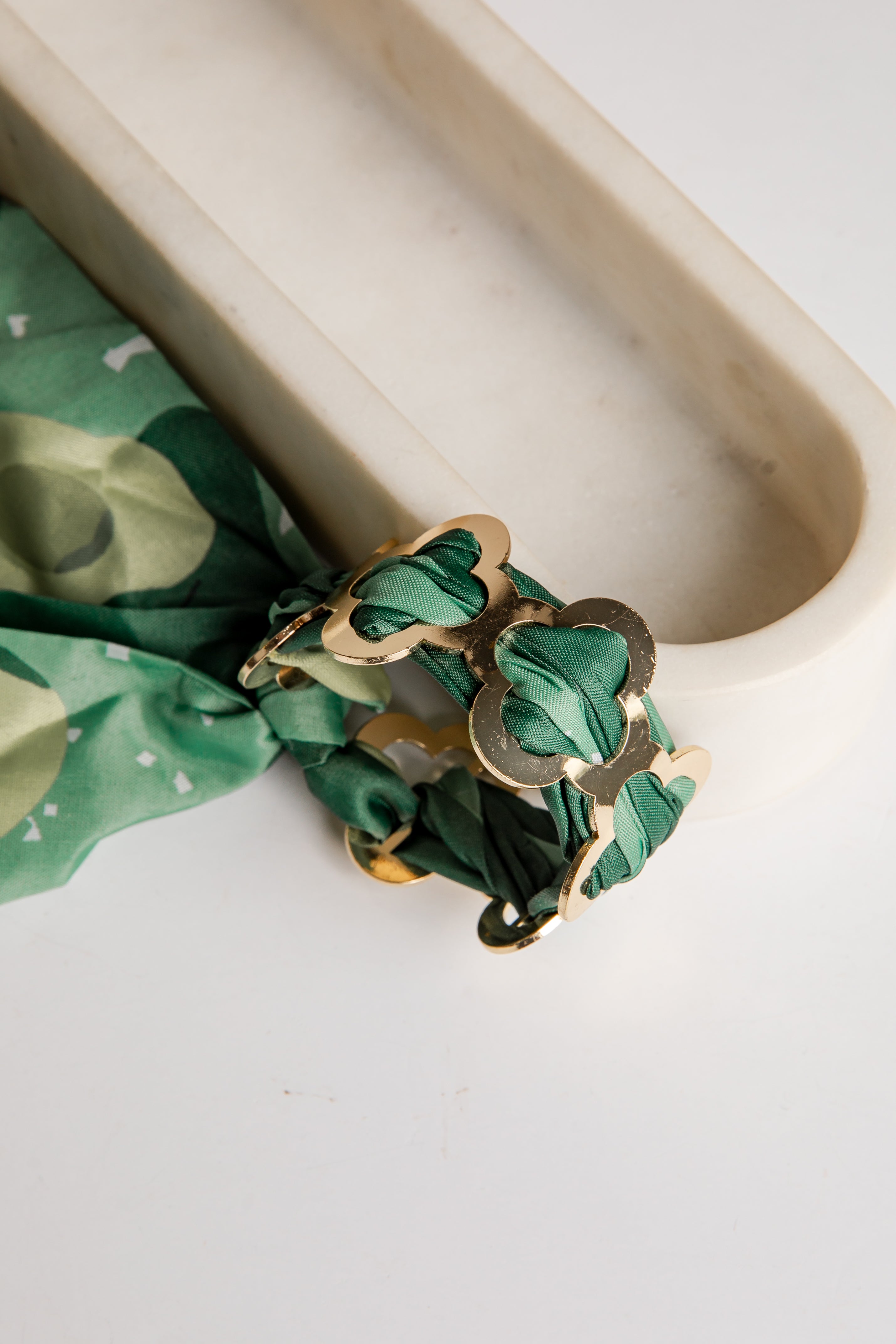 Gold bracelet with green fabric on a white surface