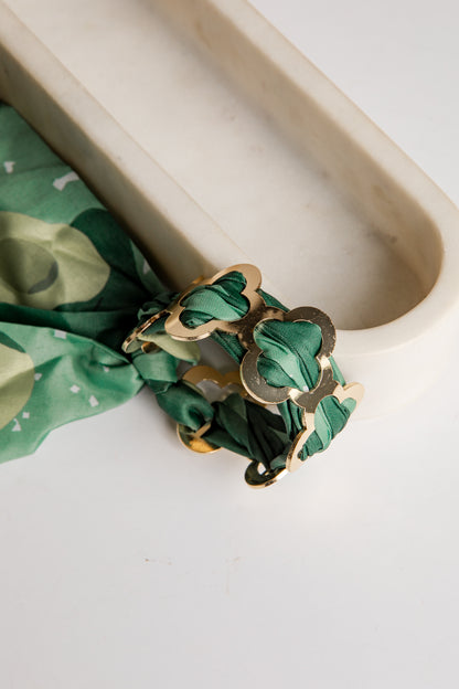Gold bracelet with green fabric on a white surface