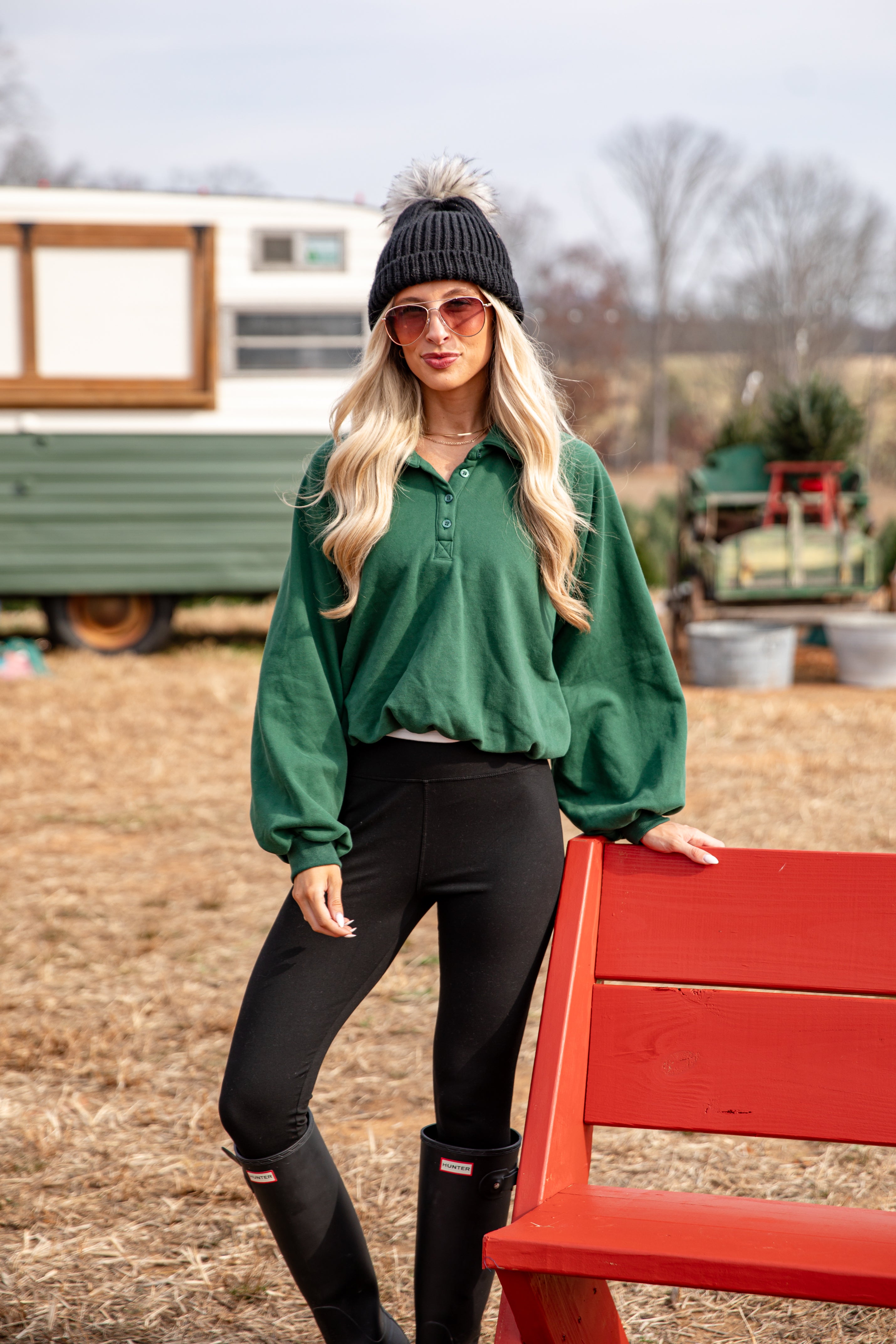 Woman in green sweater and black pants standing next to a red bench outdoors.