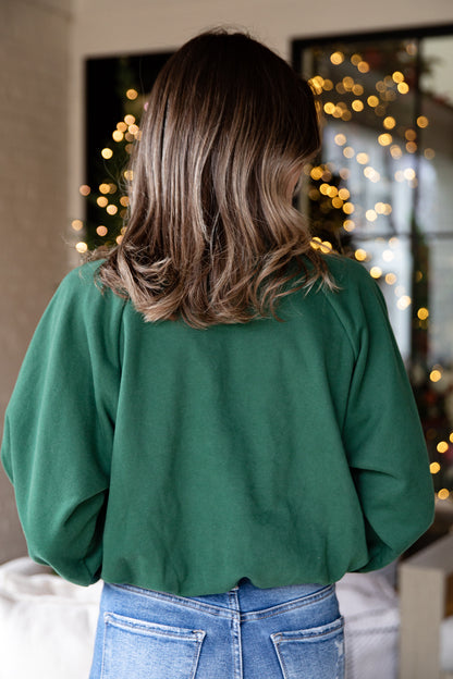 Person wearing a green sweater and blue jeans with a blurred festive background