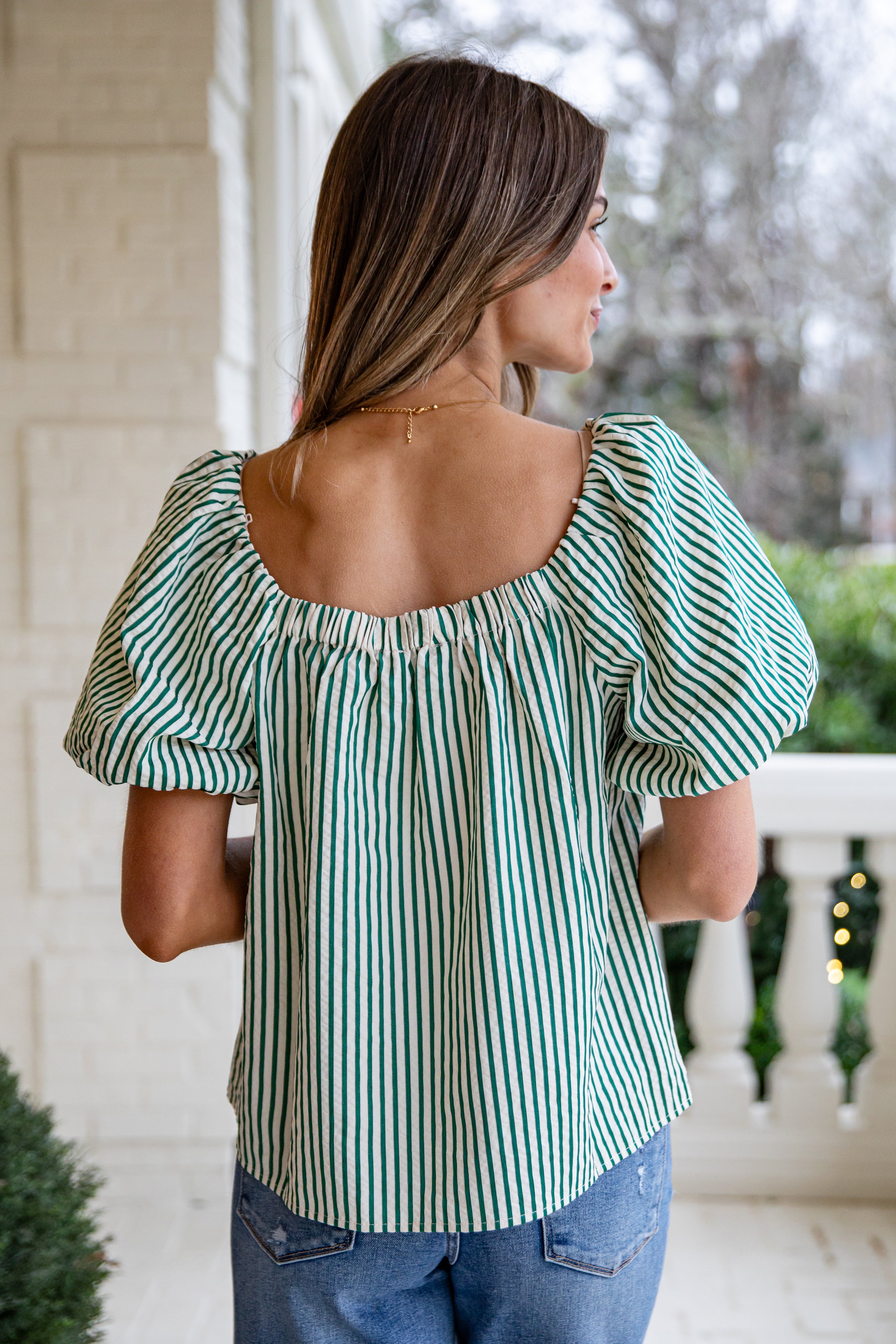 Woman wearing a green and white striped blouse on a porch