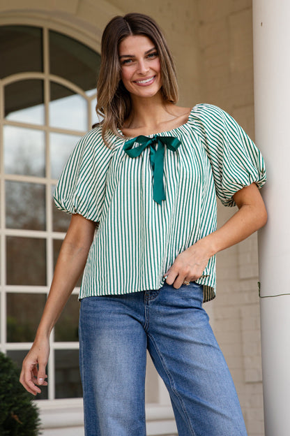 Woman wearing a green and white striped blouse with a bow tie, standing outdoors.