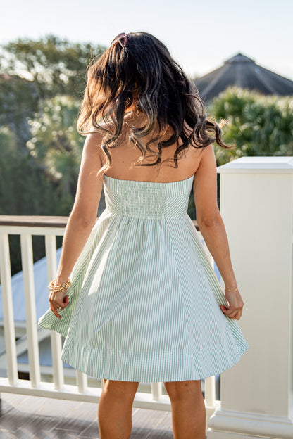 Woman wearing a light blue striped dress on a balcony with greenery in the background