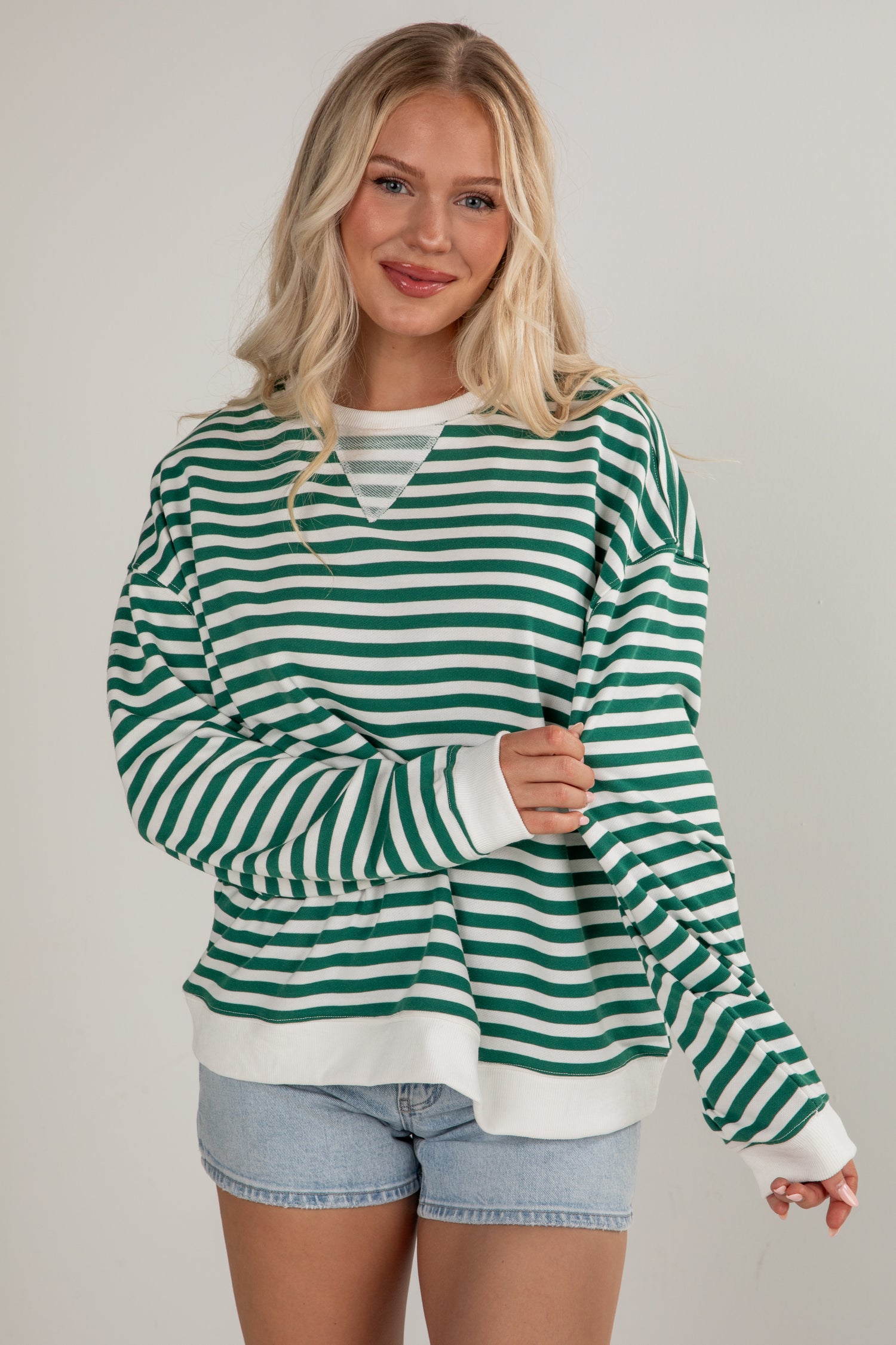 Woman wearing a green and white striped sweater with denim shorts on a plain background