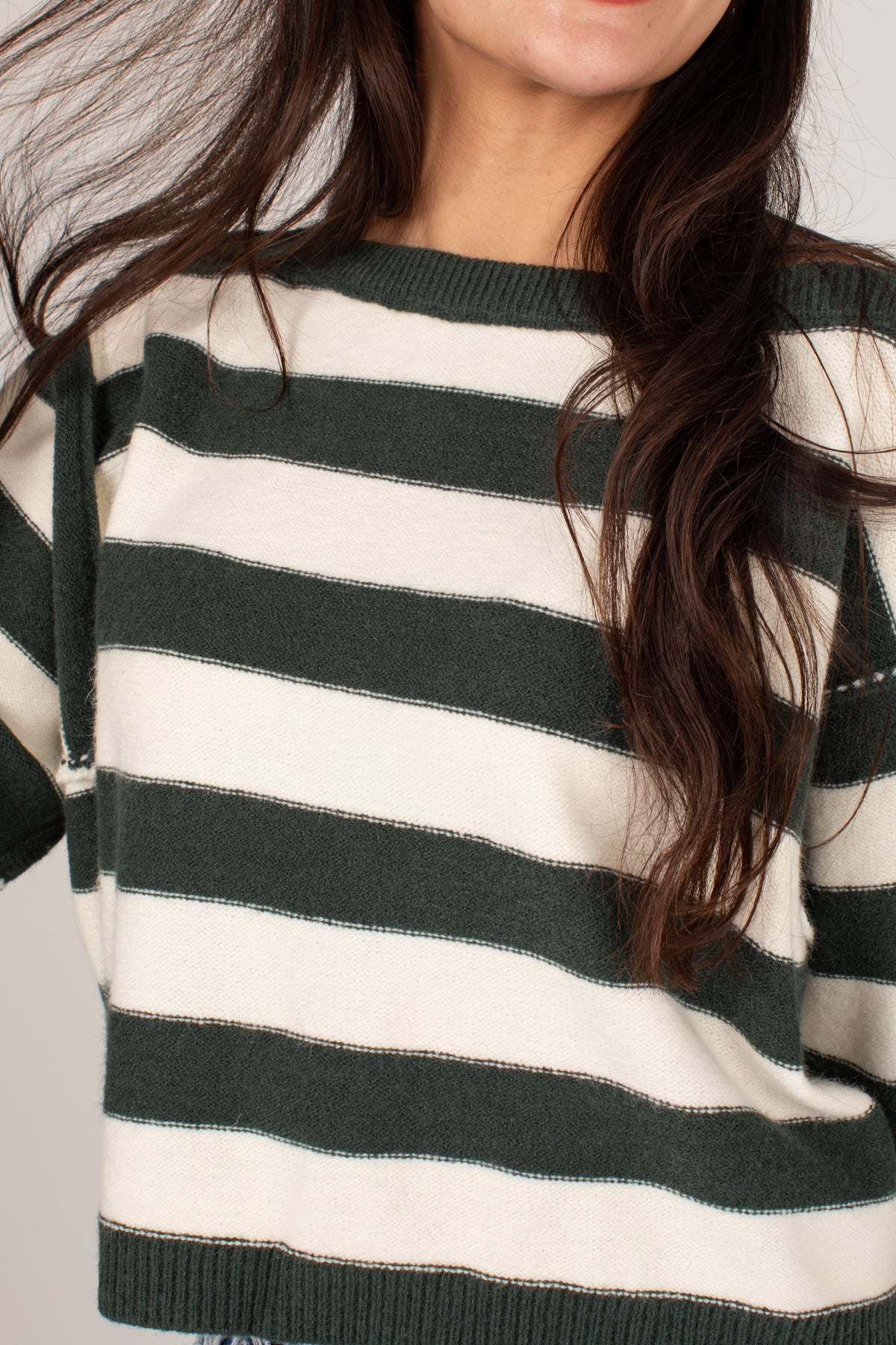 A close-up of a woman wearing a knit sweater with horizontal stripes in dark forest green and cream.