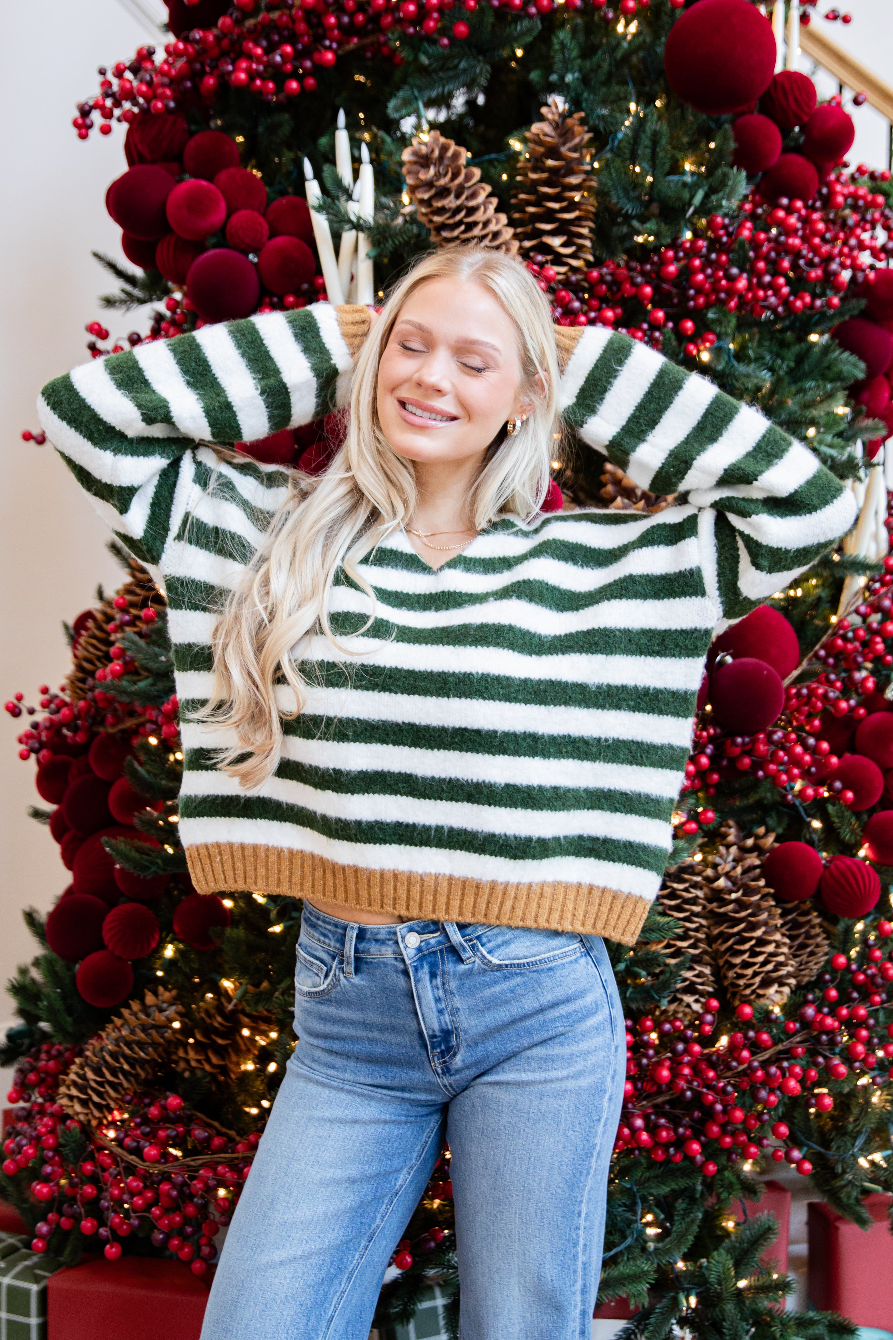 Woman wearing a green and white striped sweater in front of a decorated Christmas tree.