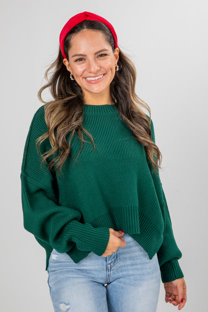 Woman wearing a green sweater and red headband against a gray background