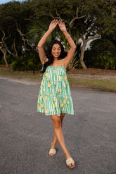 Woman in a green and yellow dress with lemon pattern standing on a road.