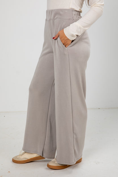 Person wearing light gray wide-leg pants with a white top on a white background