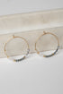 Gold hoop earrings with gray beads on a marble surface
