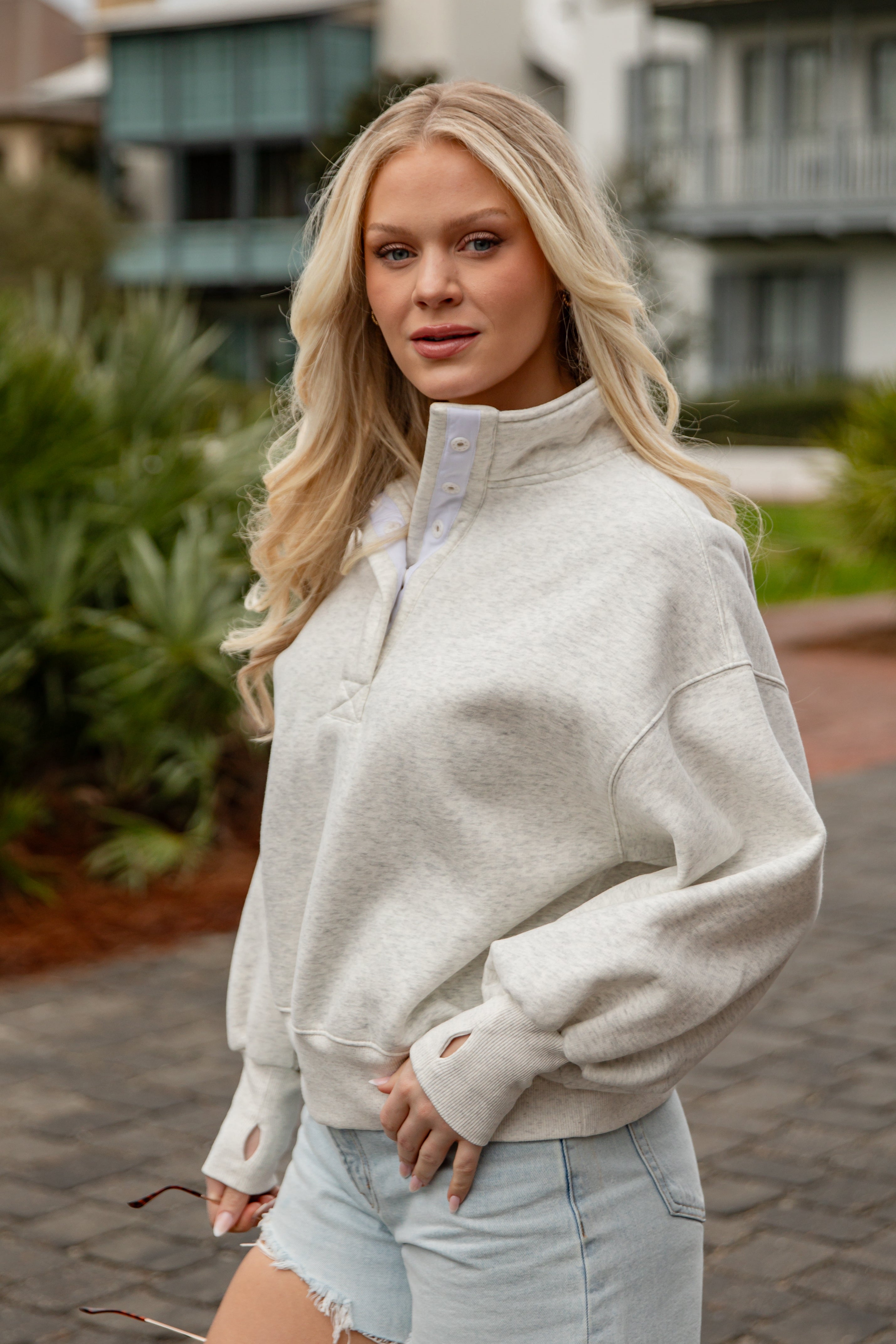 Woman wearing a light gray sweatshirt and denim shorts outdoors.