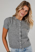 A woman wearing a gray short-sleeve button-up knit cardigan sweater and light blue jeans, photographed against a plain light gray studio background.