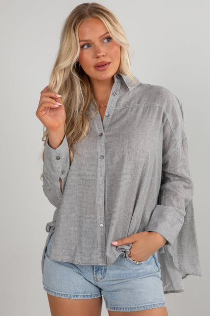 Woman wearing a gray button-up shirt and denim shorts on a plain background