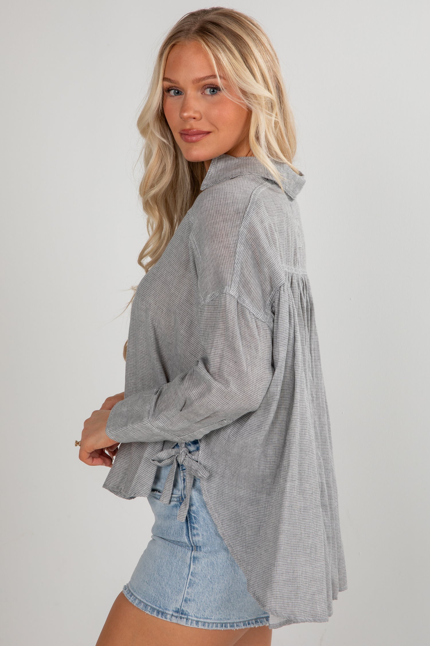 Woman wearing a gray long-sleeve shirt with a denim skirt on a plain background
