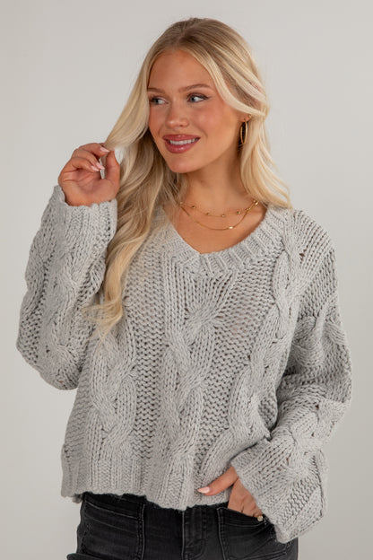 Woman wearing a gray cable knit sweater against a plain background