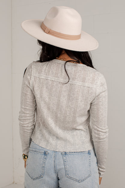 A woman shown from behind wearing a light gray ribbed knit long-sleeve top, light blue jeans, and a cream wide-brim fedora hat with a tan band.