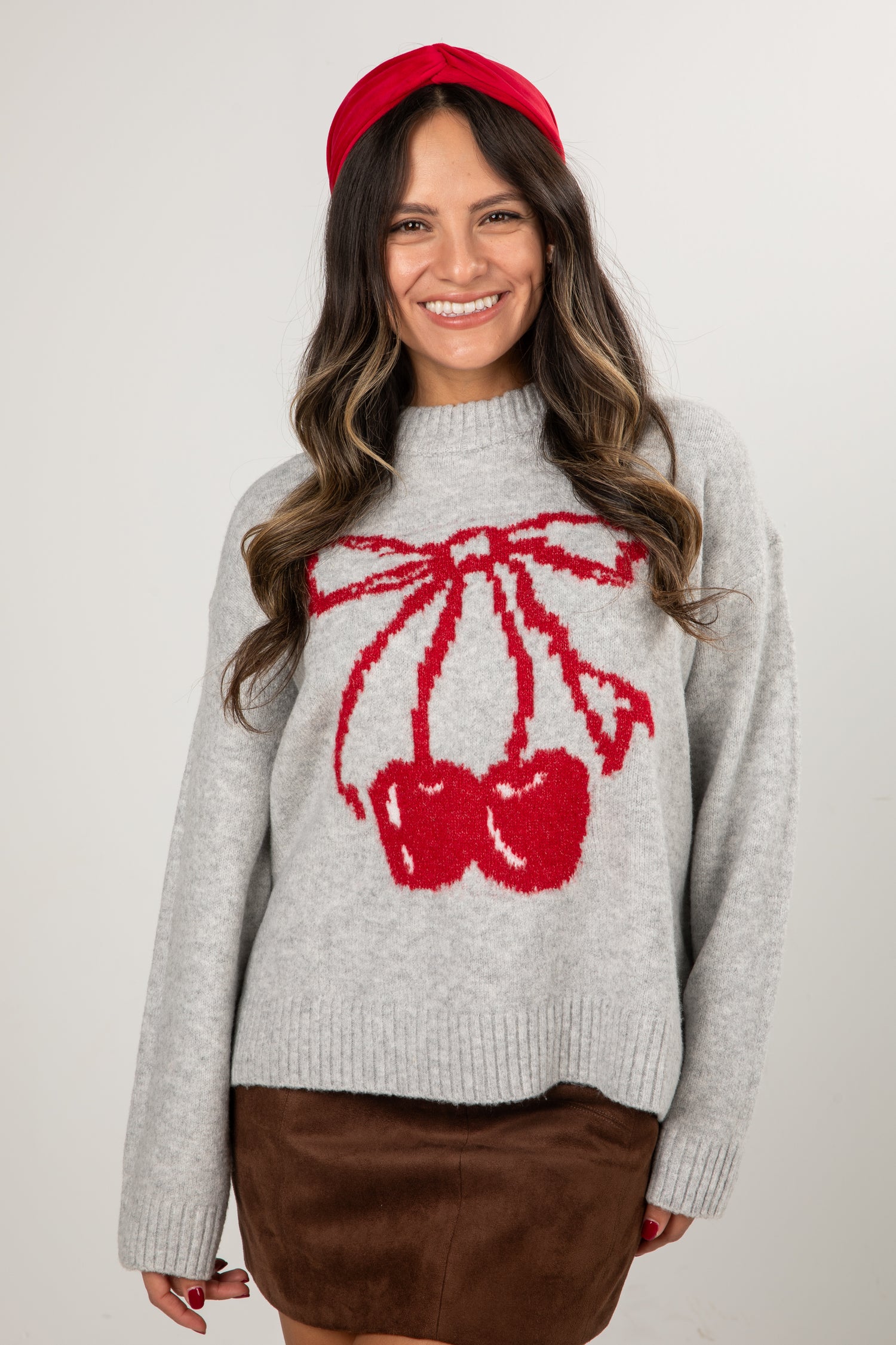 Woman wearing a gray sweater with a red bow design and a red headband against a white background