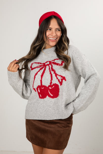 Woman wearing a gray sweater with red cherry design and a red headband against a white background