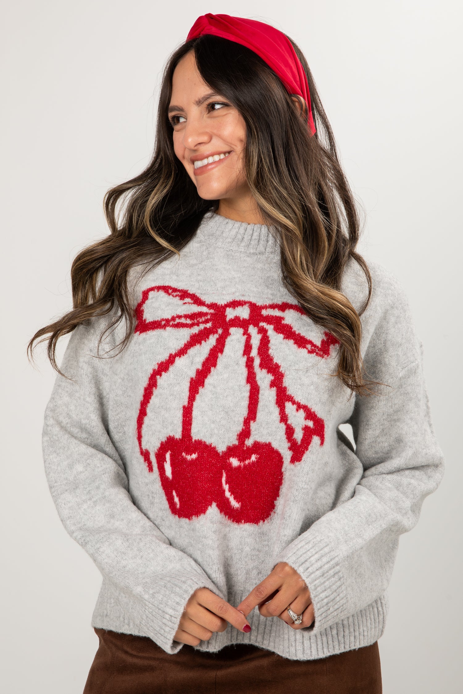 Woman wearing a gray sweater with red cherry design and a red headband against a white background